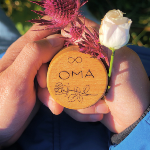 MEMENTOVIA Box in den Händen gehalten mir Gravur Rose und Unendlichkeitsschleife und dem Schriftzug OMA.