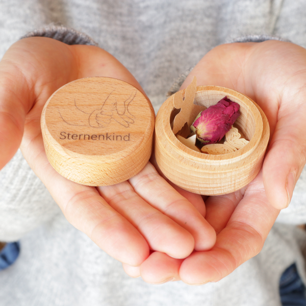 MEMENTOVIA Box geöffnet in den Händen gehalten mit symbolischen Beigaben.
