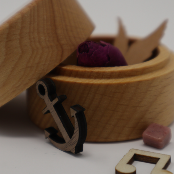 Geöffnete MEMENTOVIA-Box von der Seite, Deckel angelehnt, man sieht einige Items, eine Musiknote, einen Anker, eine Rose, die Flügel eines Engels, einen Heilstein (Rhodonit).