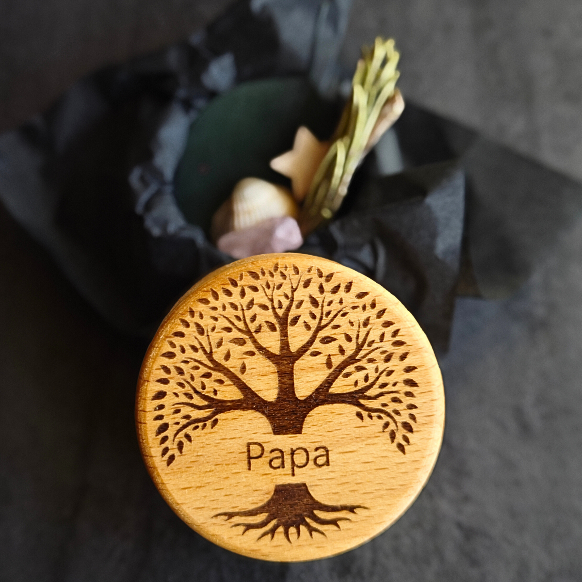 MEMENTOVIA-Box "Ewiges Band" mit Rosenquarz, Stern, Muschel, Eukalyptus und Rosmarin – Beigaben, die Liebe, Treue und die immerwährende Verbindung zum Verstorbenen symbolisieren. Mit Deckel, auf dem ein Baum-Motiv graviert ist, der Schriftzug "Papa" ist zu sehen. Die Beigaben befinden sich in schwarzem Seidenpapier.
