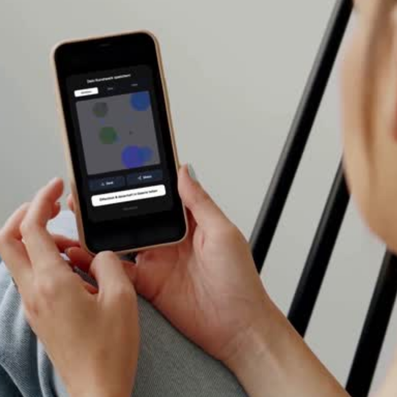 Blick über die Schulter auf ein Smartphone mit der MEMENTOVIA App. Das Display zeigt ein fertig generiertes Seelenbild im 'Bubbles'-Stil. Moderne Trauerbegleitung durch digitale Visualisierung von Gefühlen im Alltag.