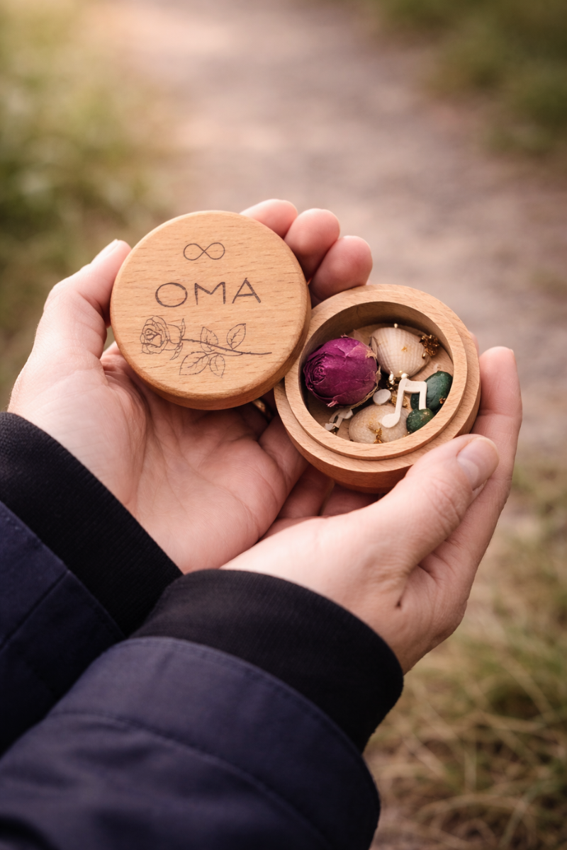 Geöffnete MEMENTOVIA Box mit personalisierter "Oma"-Gravur und symbolischen Trauer-Beigaben.